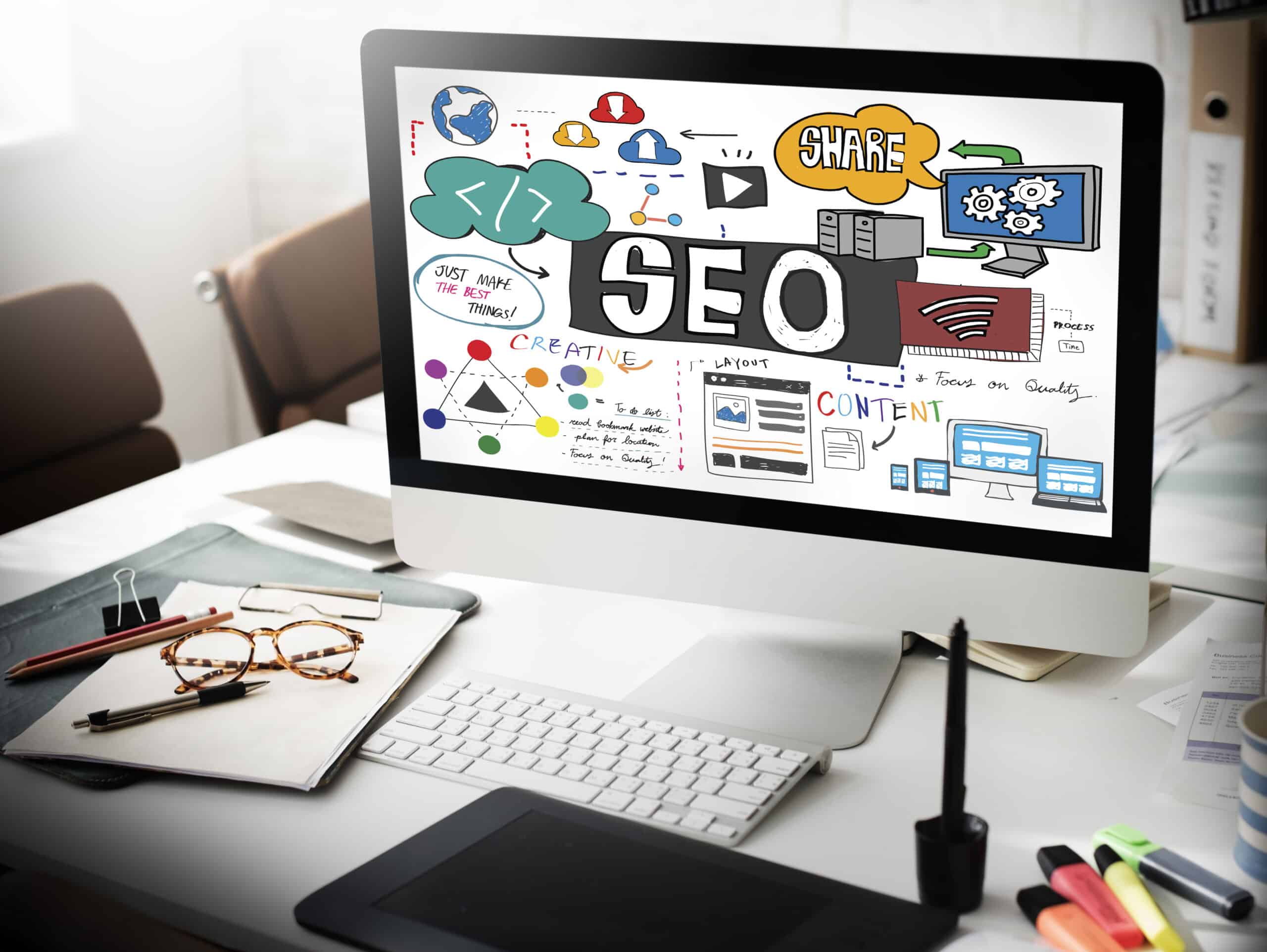 A computer screen on a desk displays colorful graphics and charts related to SEO, including tips to optimize anchor texts for better Anchor SEO. The desk has glasses, papers, a notebook, and various office supplies.