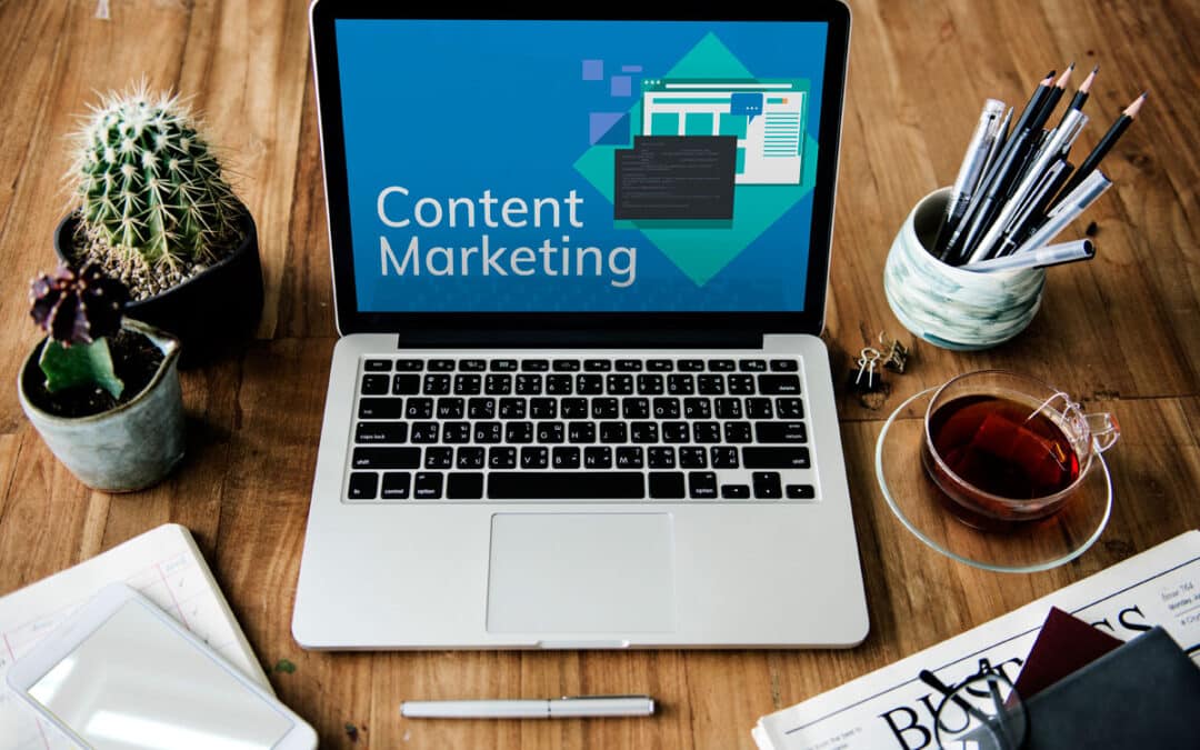A laptop on a wooden desk displays content marketing on the screen, highlighting its impact on ROI. Surrounding items include a cactus, cup of tea, pens in a holder, smartphone, notebook, and various papers.