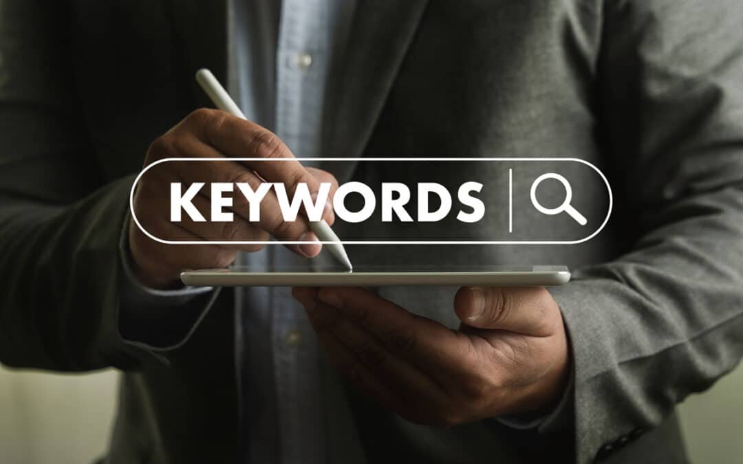 A person in a suit holds a tablet and uses a stylus. The word KEYWORDS with a search icon is overlaid, resembling an online search bar—perfect for illustrating keyword research or an SEO 2025 guide.