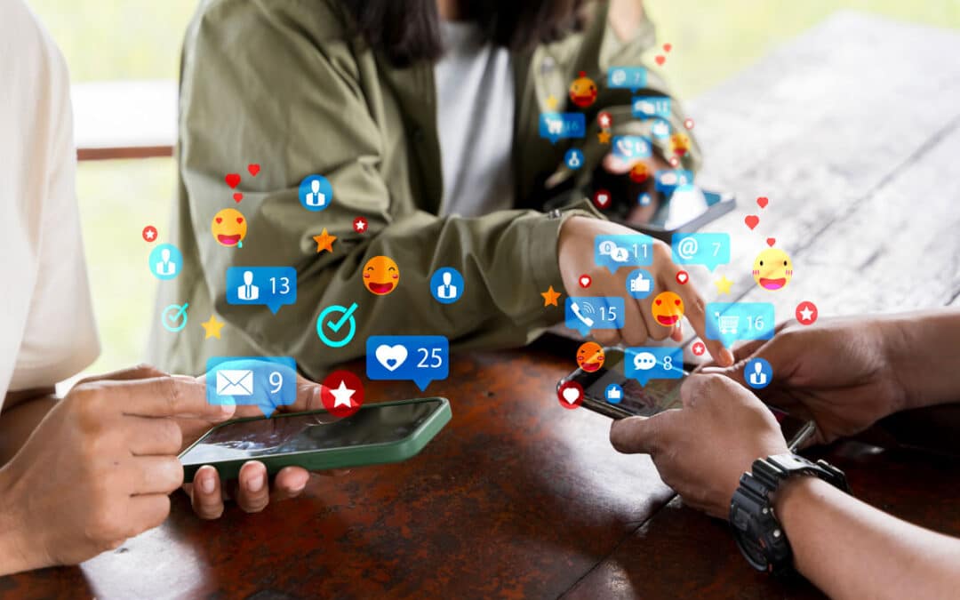 Three people using smartphones at a table, with colorful social media notification icons overlayed above their phones, highlighting 2025 best practices for an effective social media strategy.